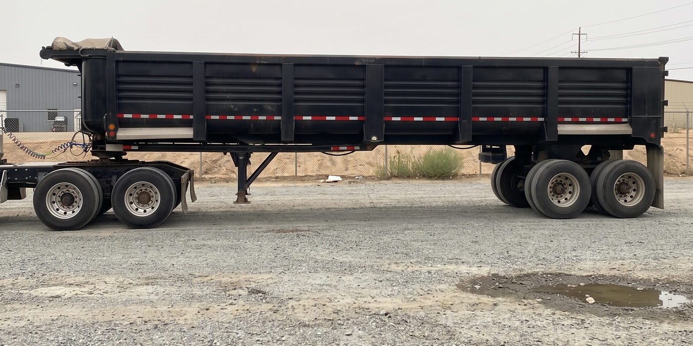 End dump trailer in side profile, hitched to a tractor in the yard