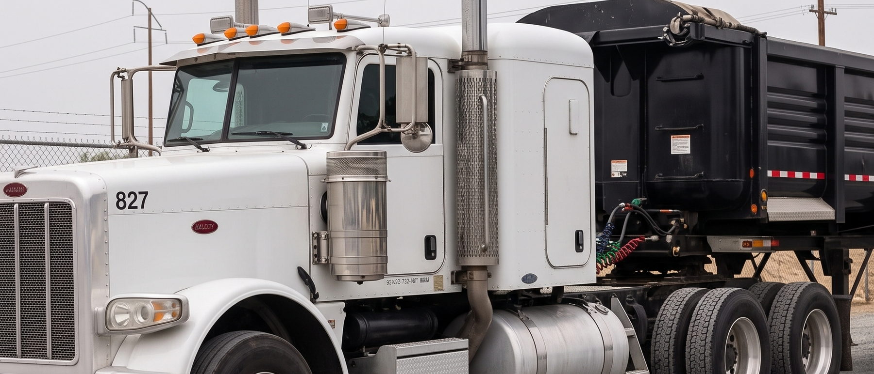 Peterbilt tractor unit 827 hitched to a black end dump trailer, staged in the yard